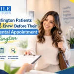 Smiling woman handing a clipboard to reception staff inside a modern dental office desk area.